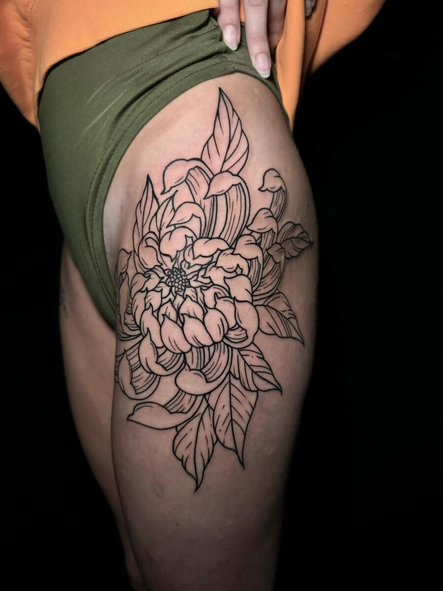 Tatuaje floral de arte lineal negro en la parte superior del muslo de una persona, sobre un fondo oscuro.