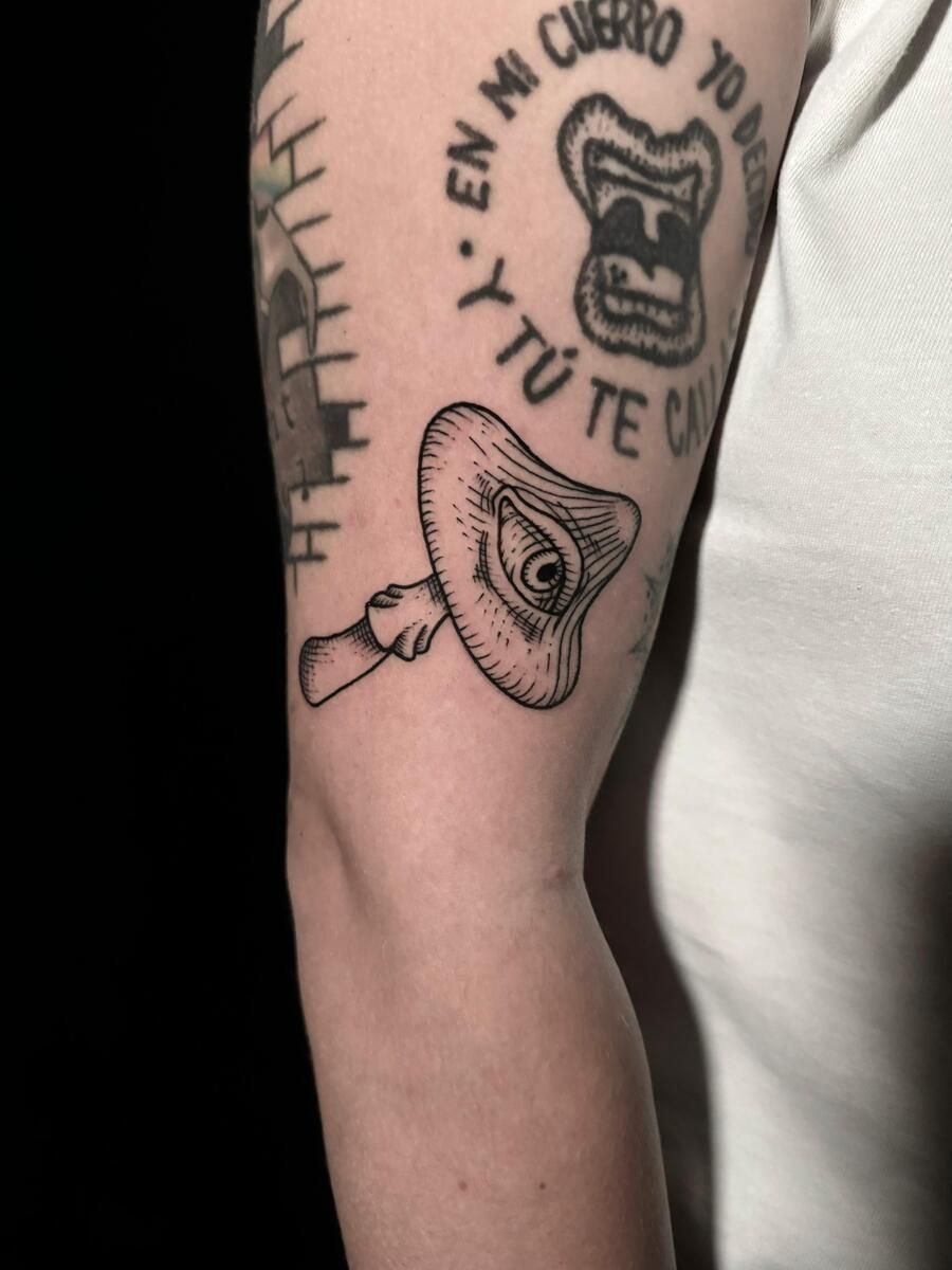 Tatuaje en el brazo de una mano sosteniendo un ojo estilizado, con otros tatuajes visibles.
