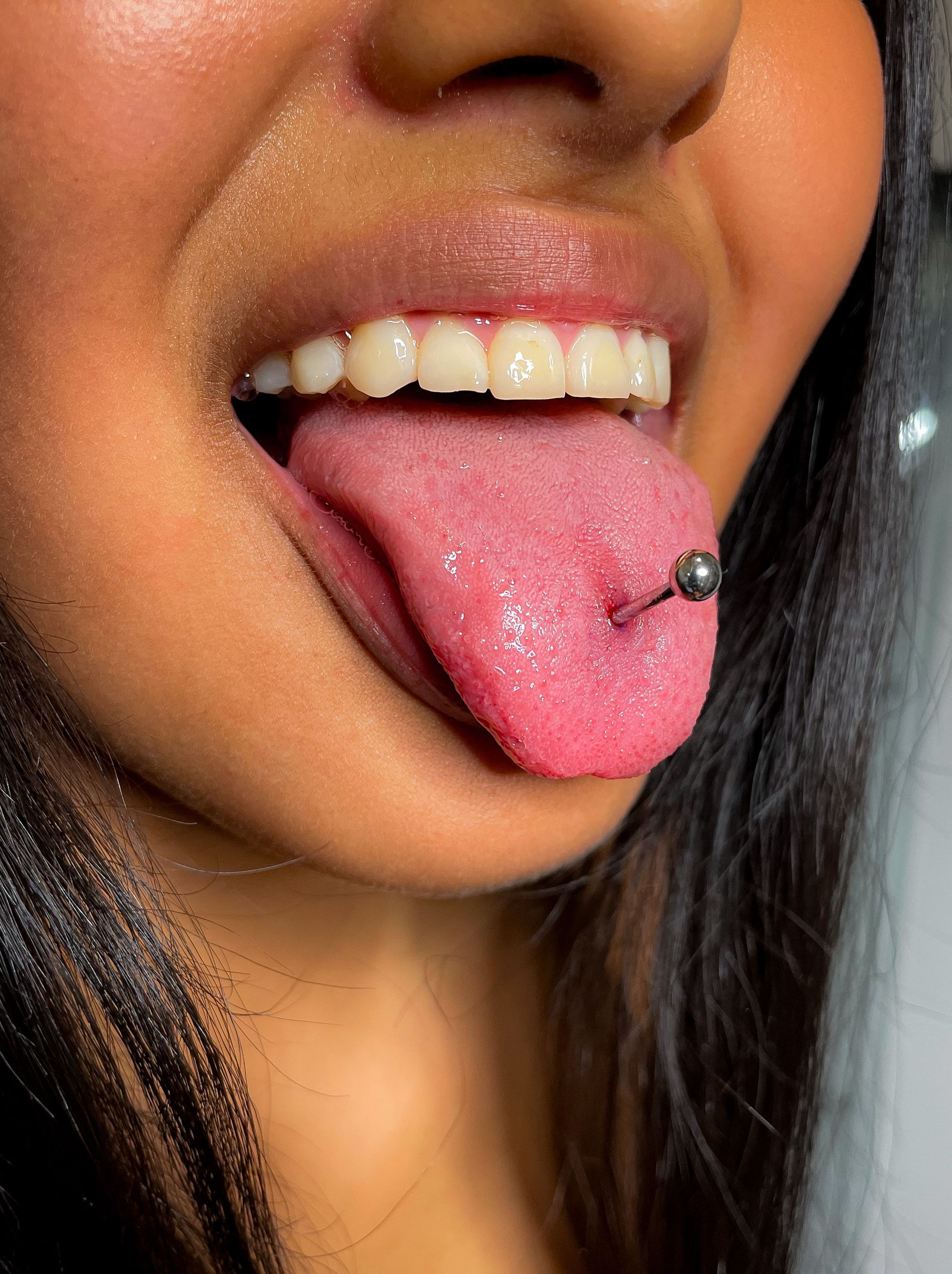 Persona con piercing en la lengua, boca abierta, lengua afuera y joya en forma de barra de plata.