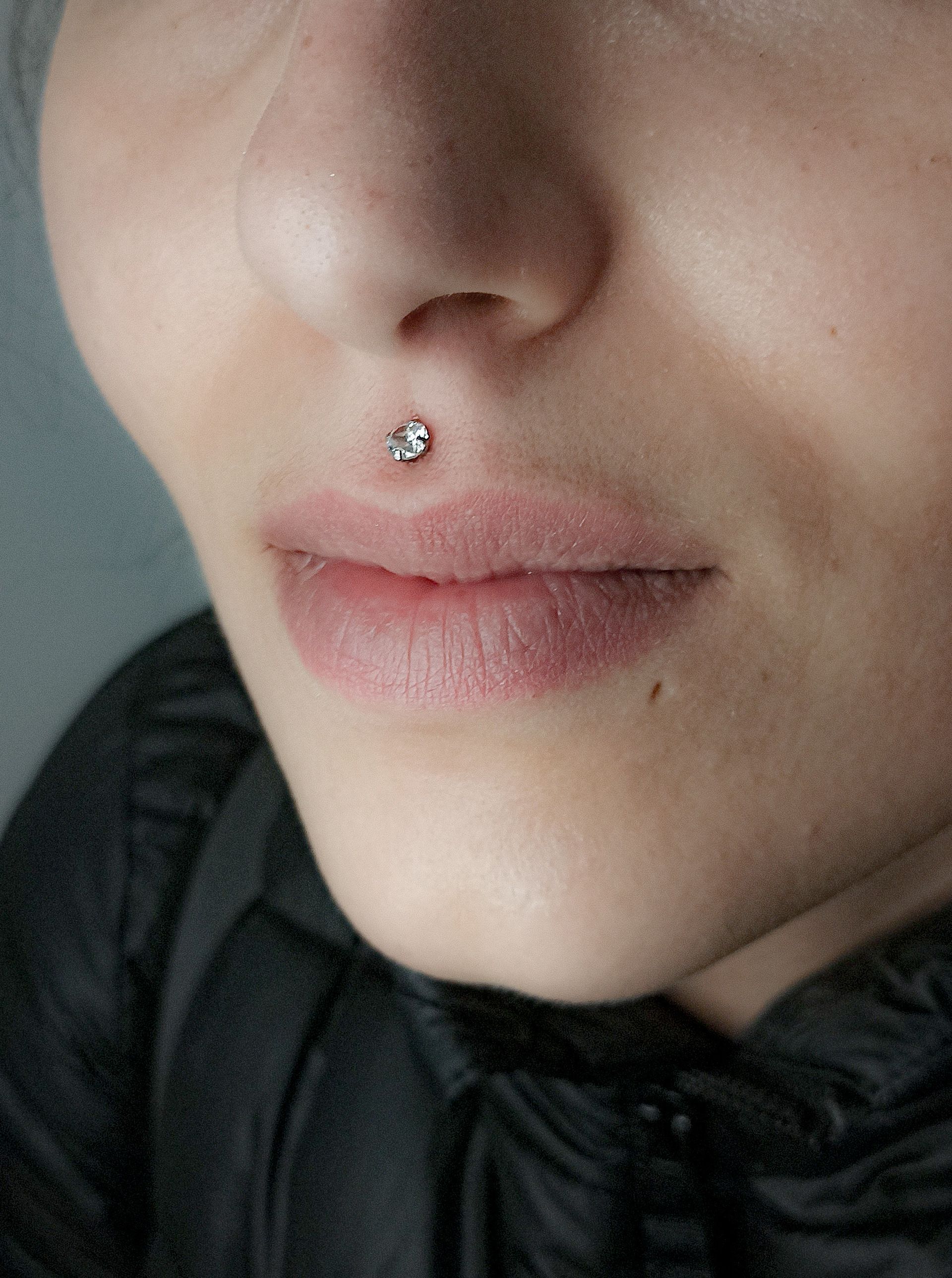 Primer plano de la cara de una persona con un piercing en el labio; un pequeño pendiente con joya encima del labio.