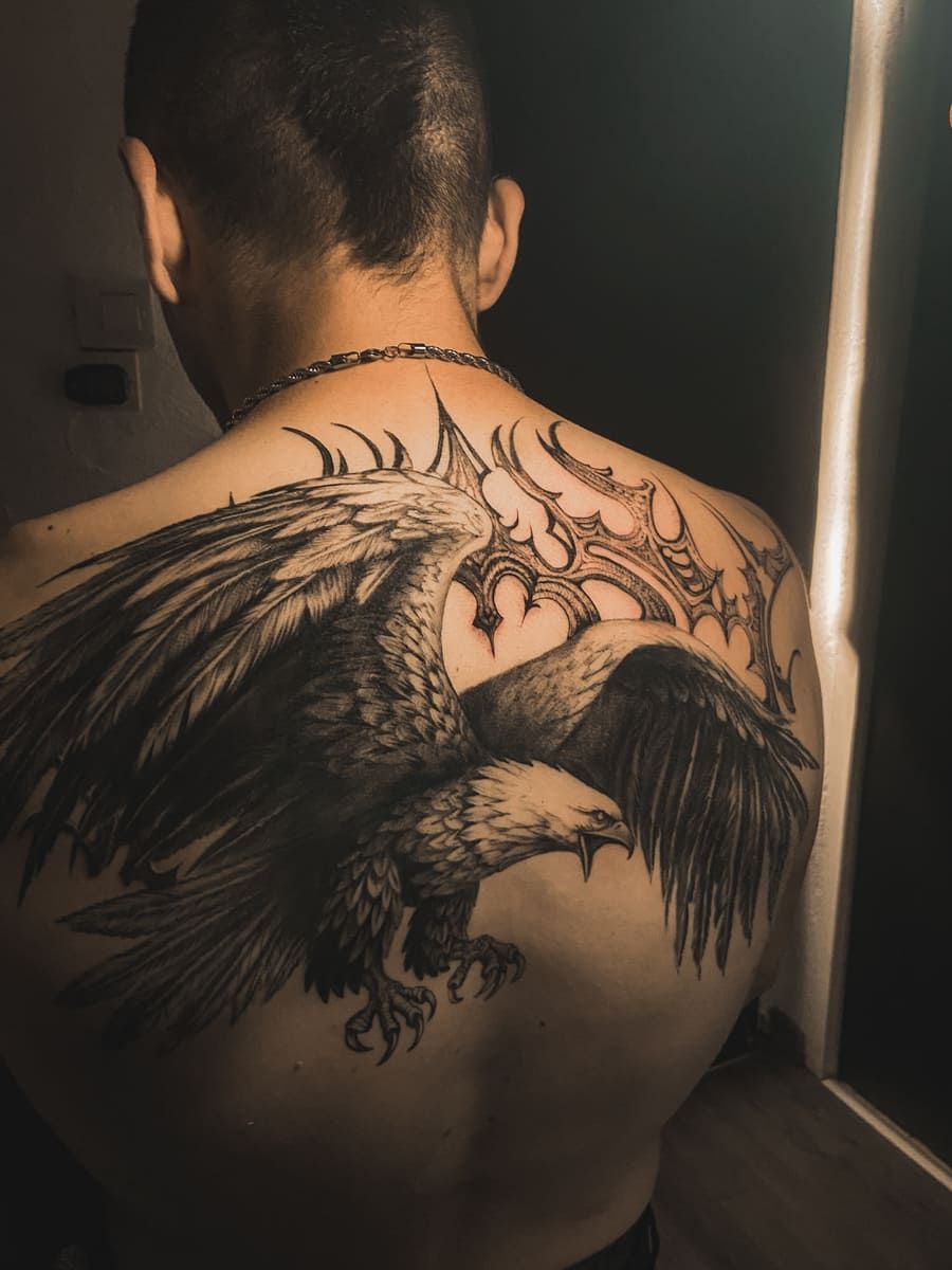 Tatuaje en la espalda de un águila con las alas extendidas y un elemento decorativo encima.