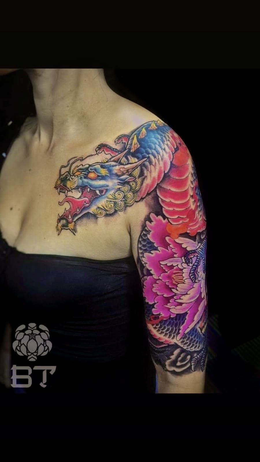 Hombro y brazo de mujer con un dragón colorido y un tatuaje floral.