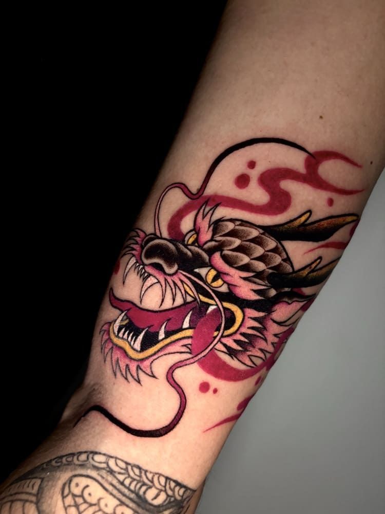 Tatuaje de cabeza de dragón en un brazo, con tinta roja y negra.