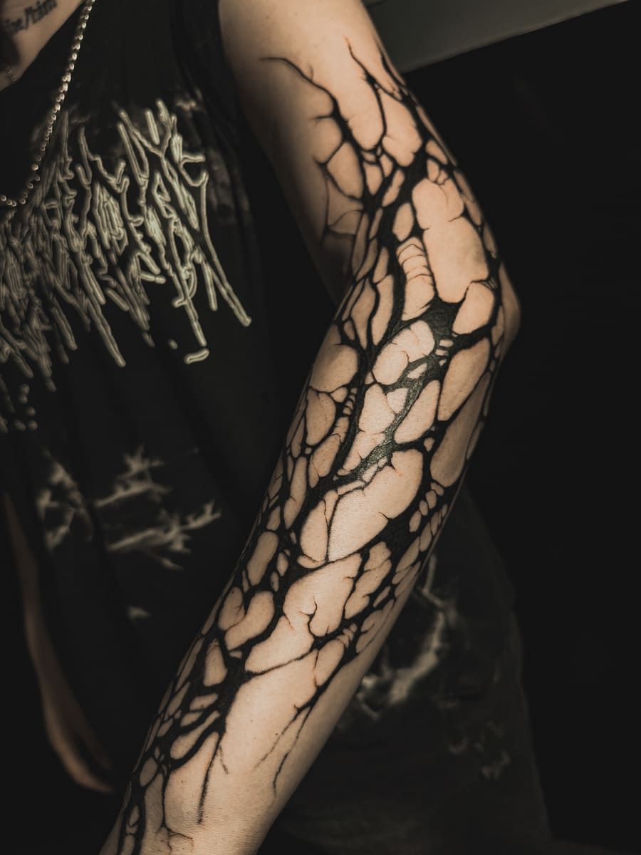 Brazo con tatuaje en forma de vena negra, sobre un fondo oscuro.