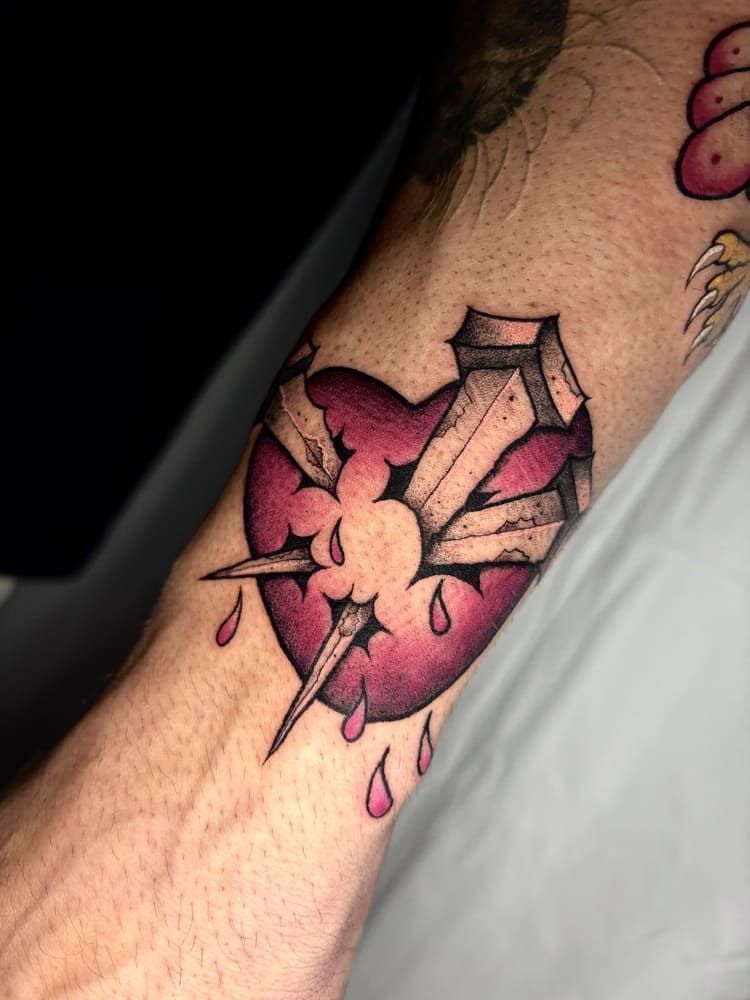 Tatuaje de un corazón roto con púas y sangre goteando en un antebrazo.