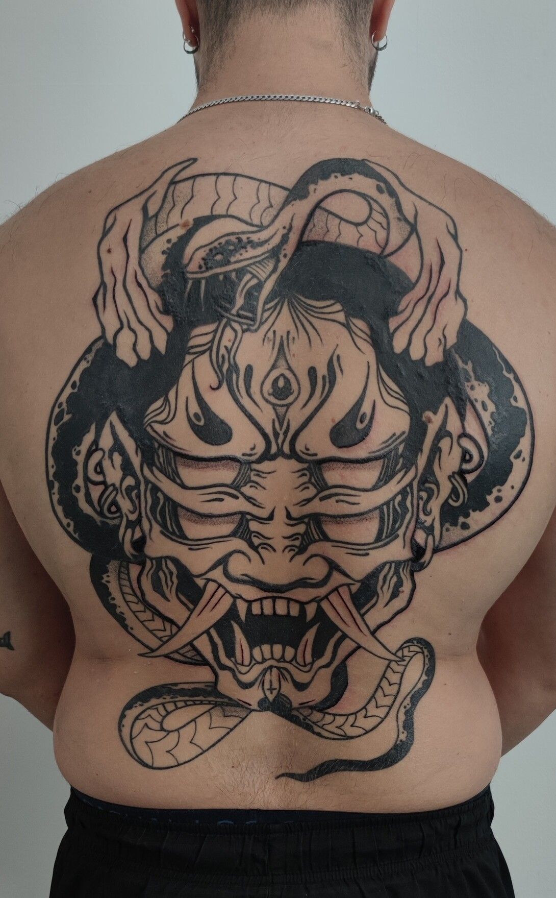 Tatuaje en la espalda de un hombre de una gran máscara de Oni negra y una serpiente.