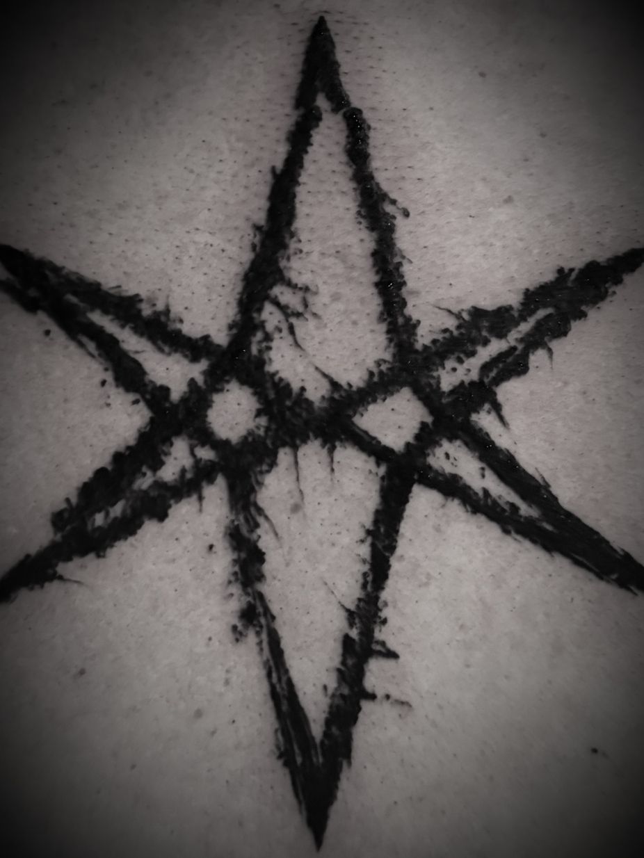 Tatuaje en forma de estrella en tinta negra, compuesto por dos triángulos que se entrecruzan, sobre la piel.