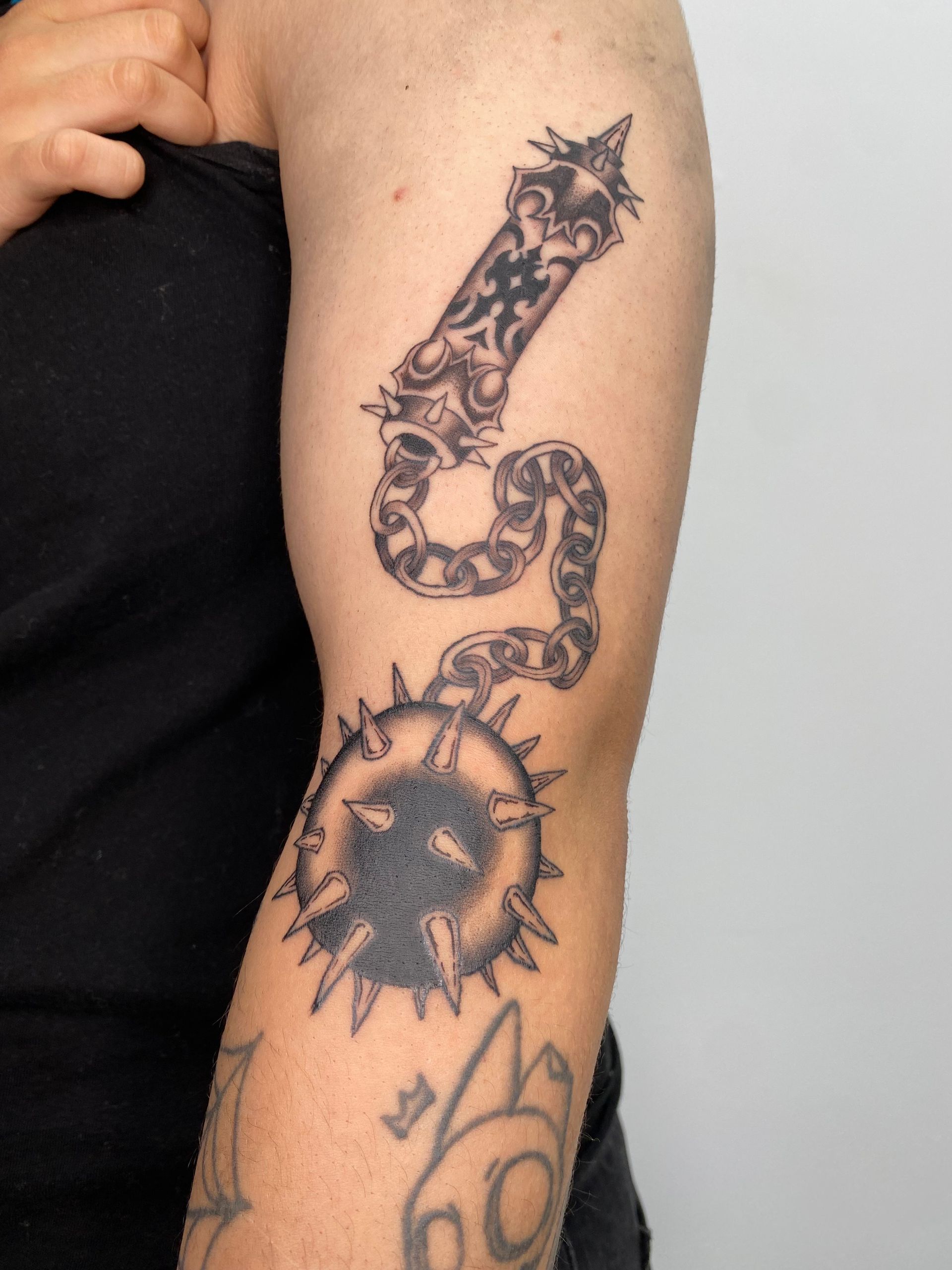 Tatuaje en la parte superior del brazo de una maza con púas y mango decorativo.