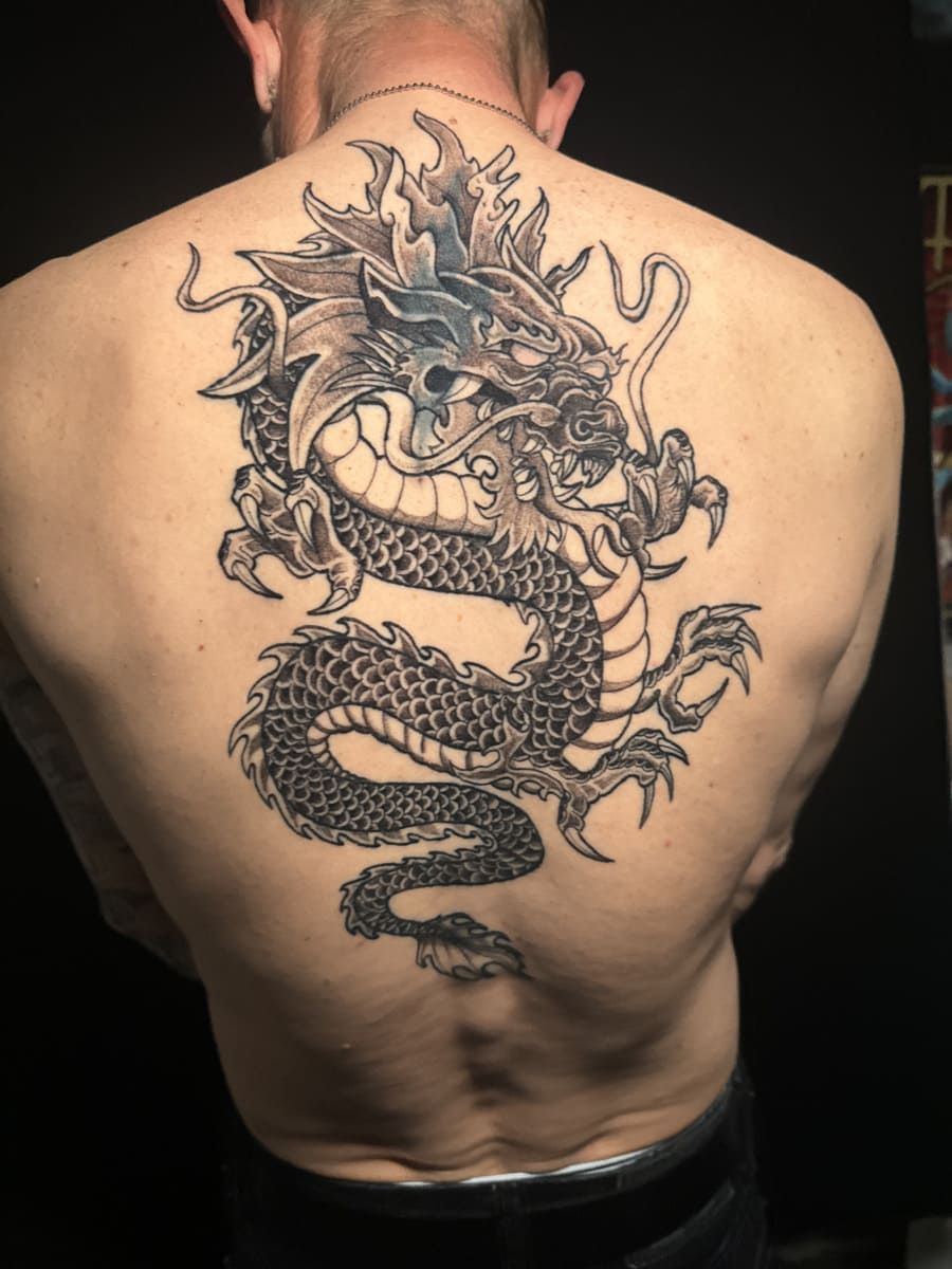 Tatuaje de dragón blanco y negro en la espalda. El dragón presenta escamas y garras, en una pose estilizada.