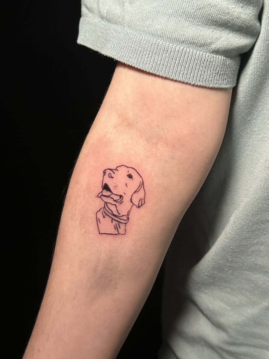 Tatuaje de un perro en la parte interna del brazo. El perro jadea y lleva collar.