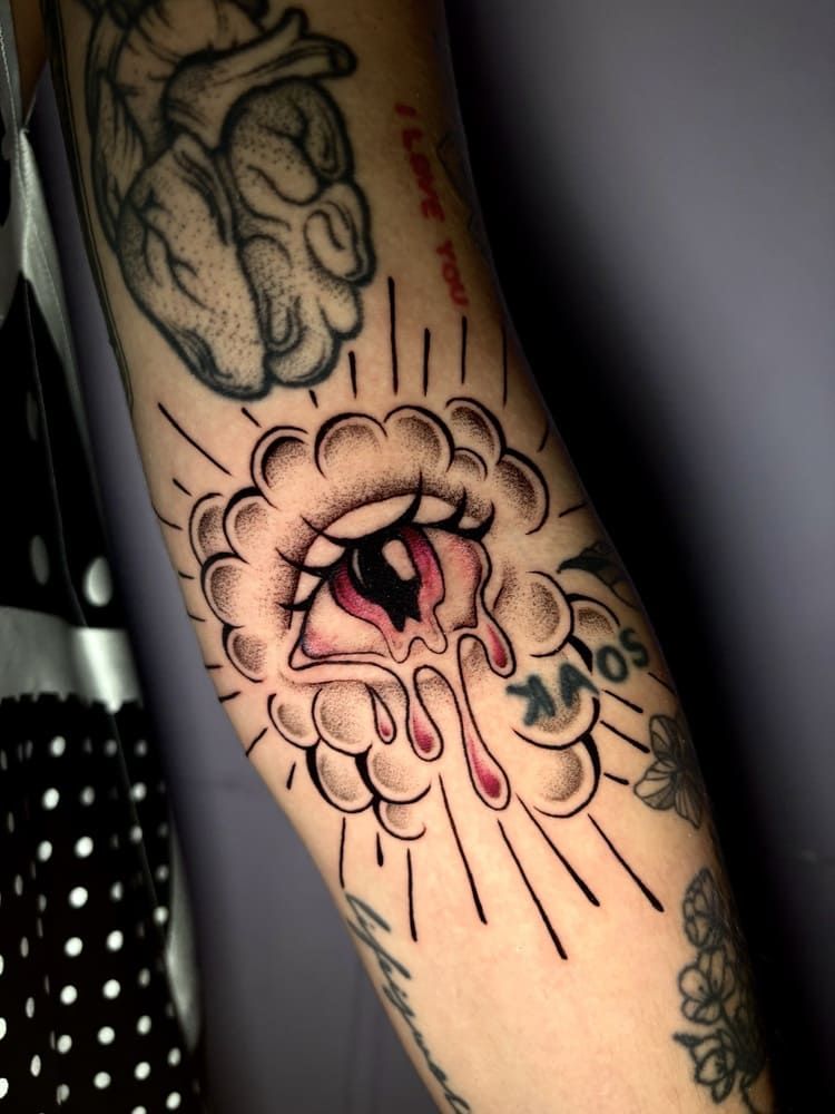 Tatuaje de un ojo sangrando, rodeado de líneas radiales. Ubicado en el brazo de una persona.