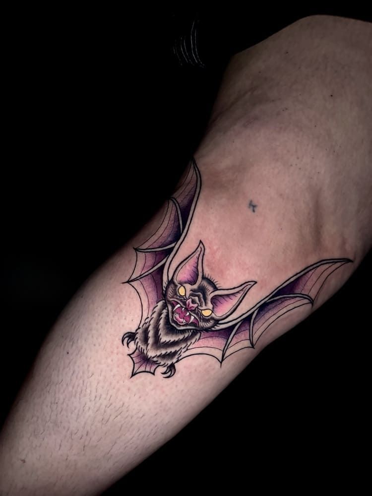 Tatuaje de murciélago en un brazo, con coloración morada y negra.