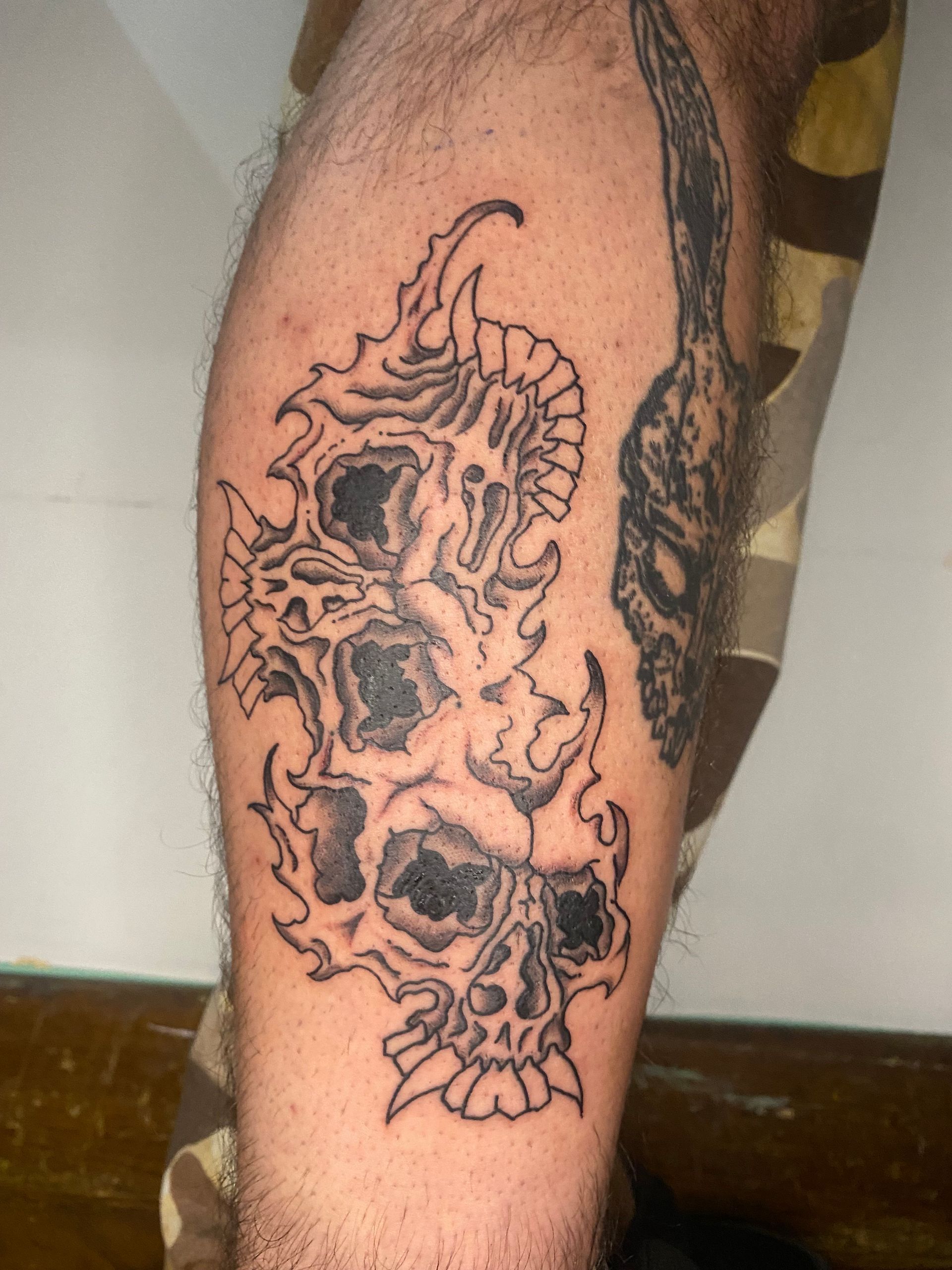 Tatuaje de tres calaveras estilizadas en una pierna. Tinta negra con sombreado.