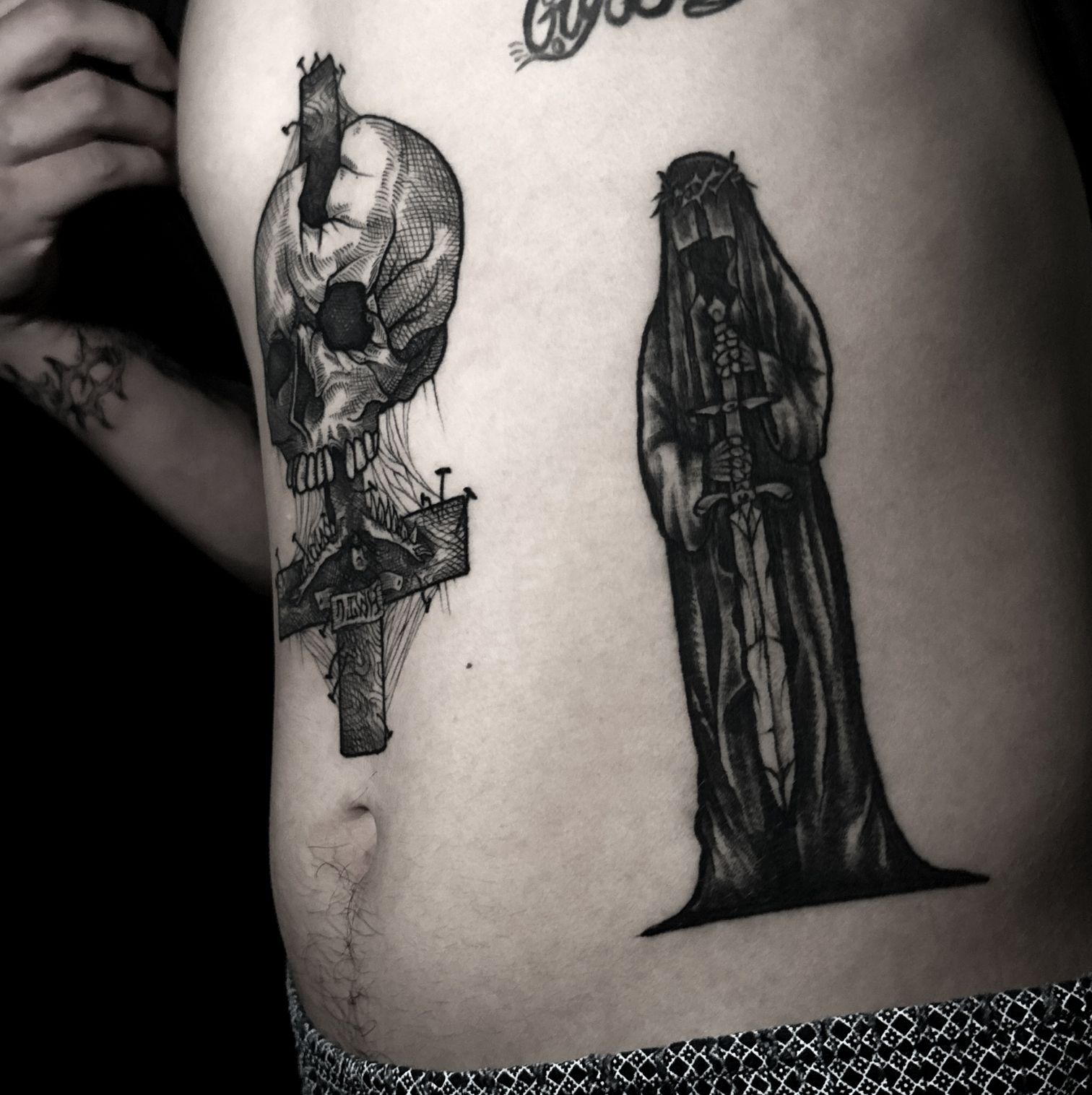 Dos tatuajes oscuros en un torso: una calavera empalada en una cruz y una figura encapuchada con una espada.