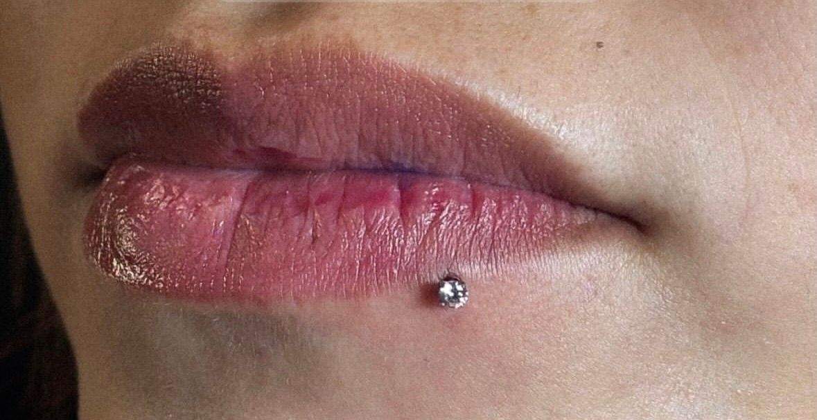 Persona perforándose la oreja con un instrumento. Manos enguantadas negras.