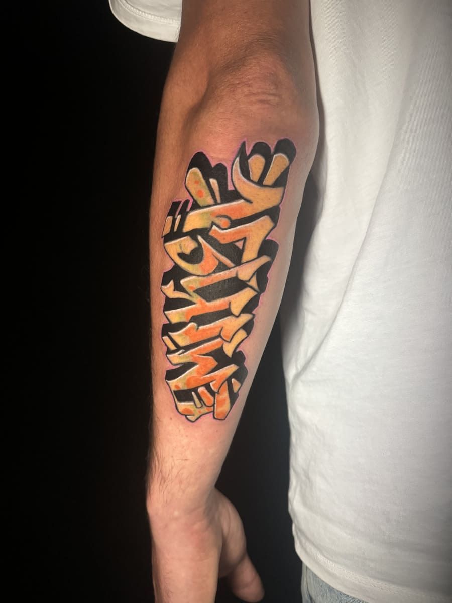 Brazo con un tatuaje estilo graffiti en color amarillo y naranja.