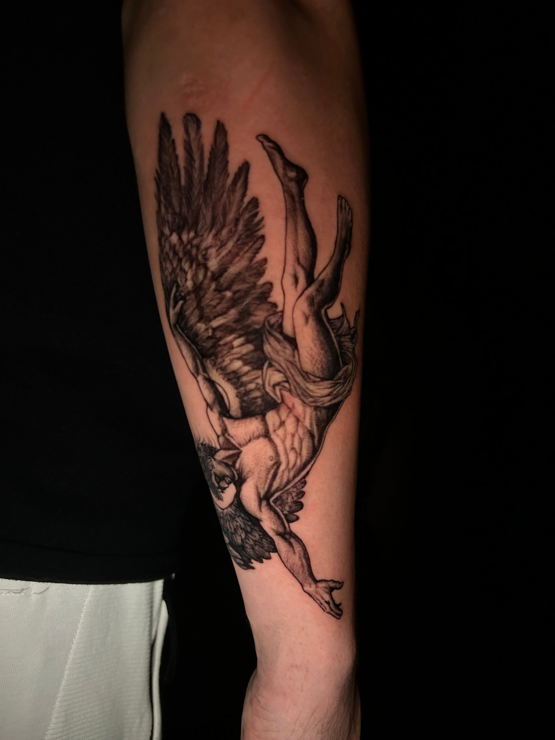 Tatuaje de una figura alada, boca abajo y cayendo, en un antebrazo.