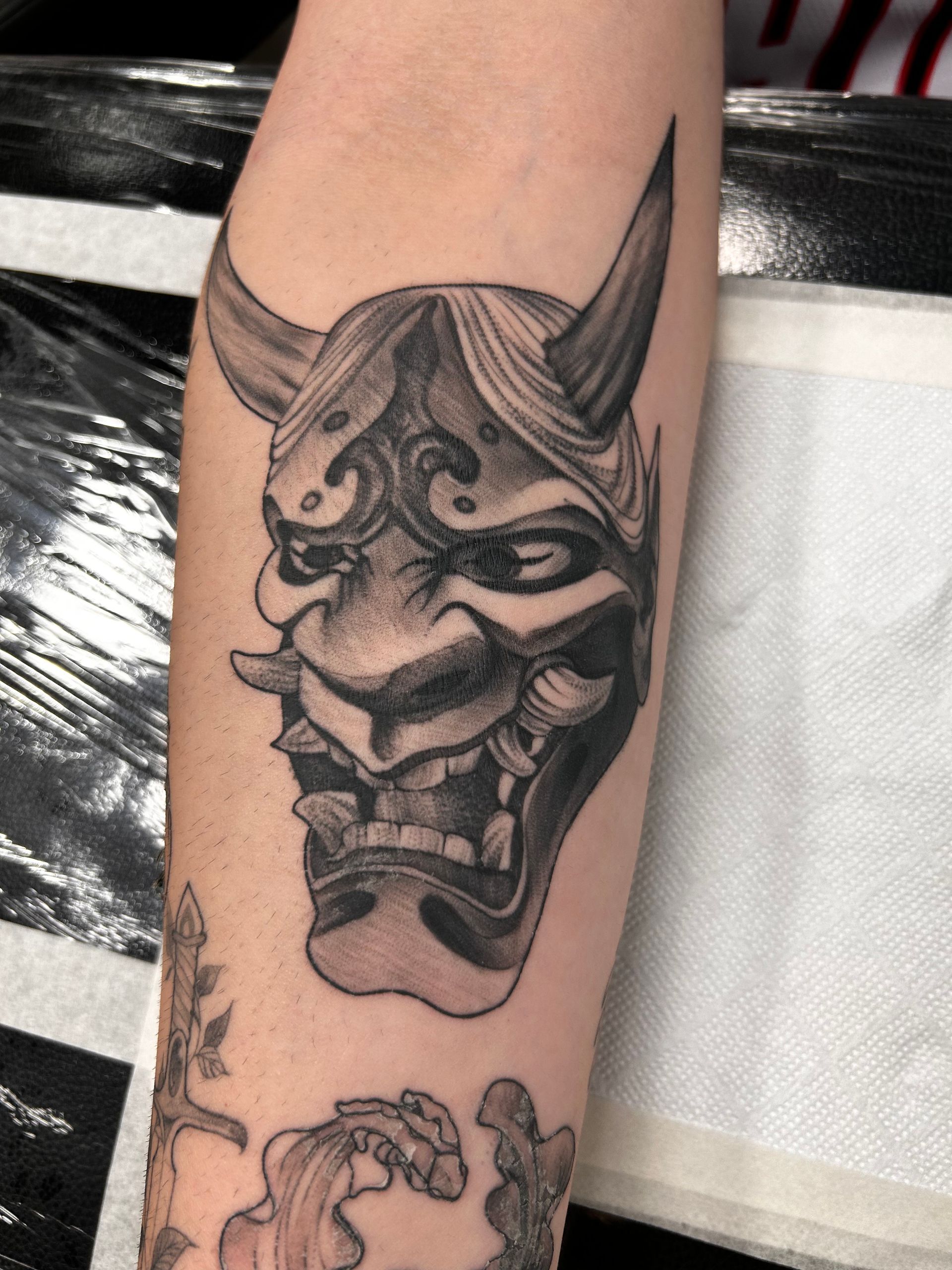 Tatuaje de una máscara Oni japonesa negra y gris en un brazo.