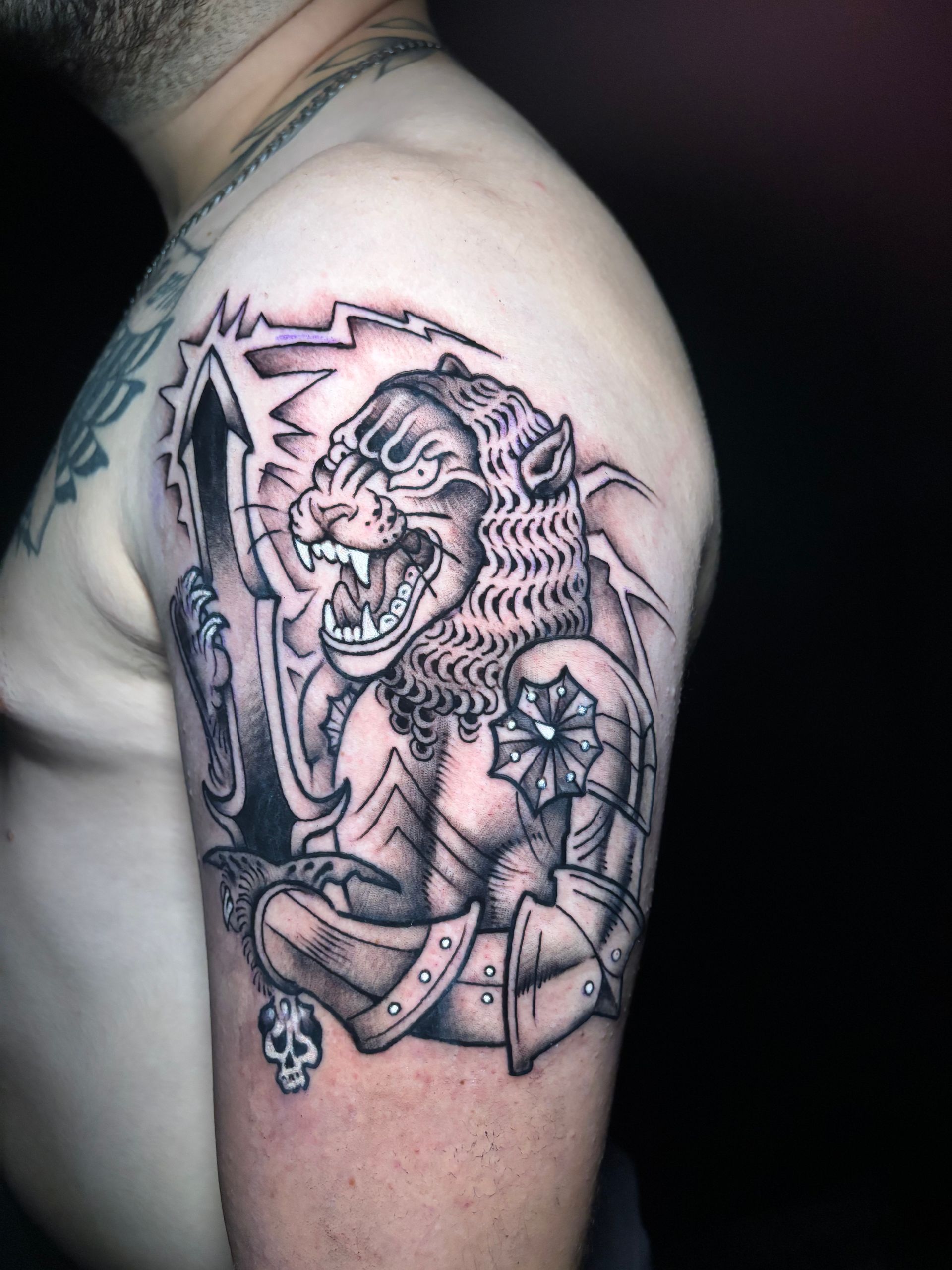 Tatuaje de un león feroz con armadura, espada en mano, con un rayo como fondo. Cráneo en la parte inferior.