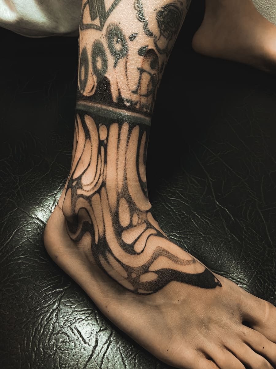 Tatuaje en el tobillo y el pie, diseño en tinta negra. Patrón abstracto y ornamentado que se extiende desde el pie.