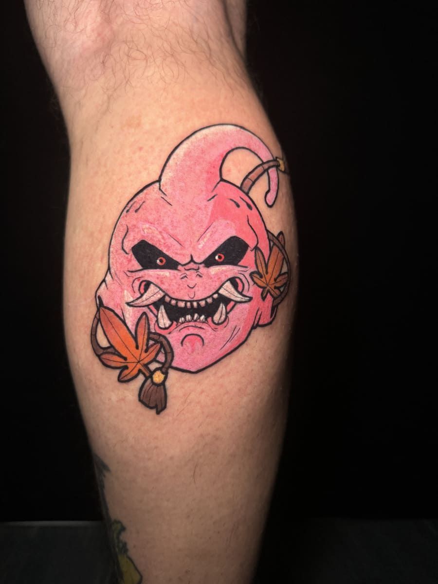 Tatuaje de un personaje Majin Buu rosa con expresión enojada, detallado con hojas de arce.