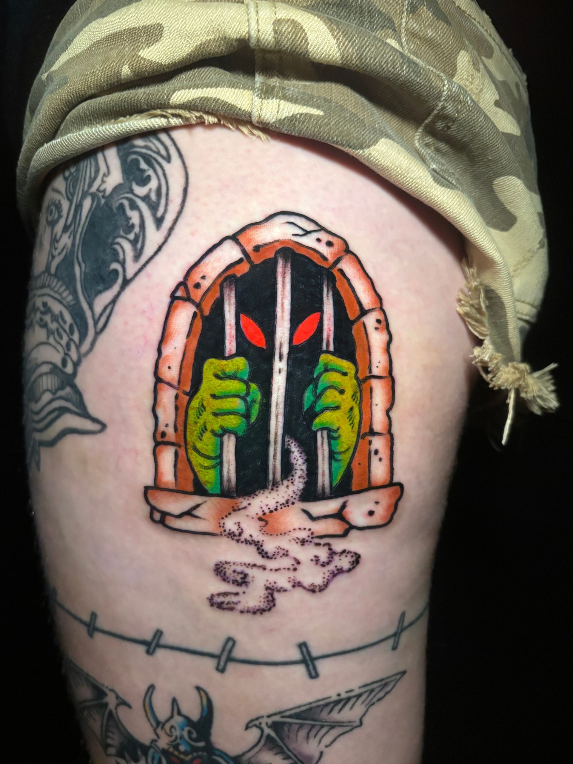 Tatuaje de un monstruo verde en una cárcel de piedra con ojos rojos y manos con garras; en una pierna.