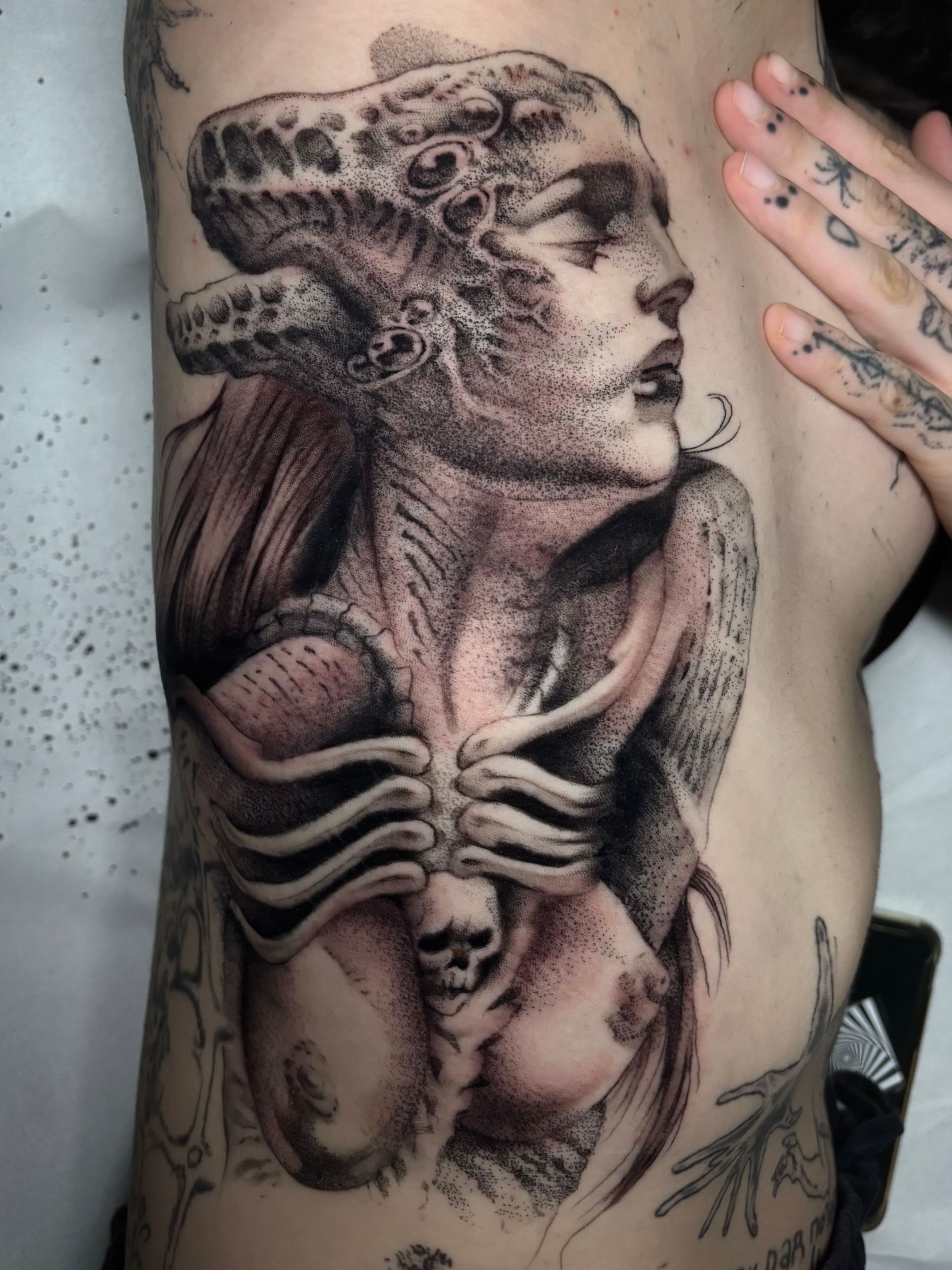 Tatuaje de una mujer con cuernos y rasgos esqueléticos en el torso de una persona.