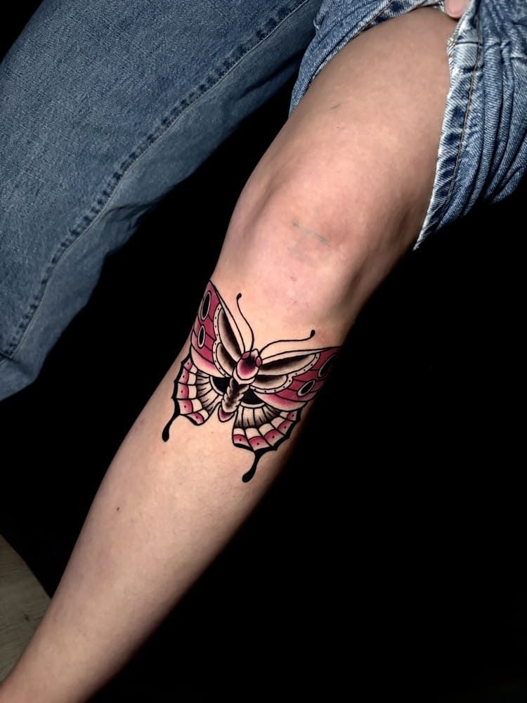 Tatuaje de mariposa en la rodilla, con alas rosas y negras y contorno negro. Persona con vaqueros.