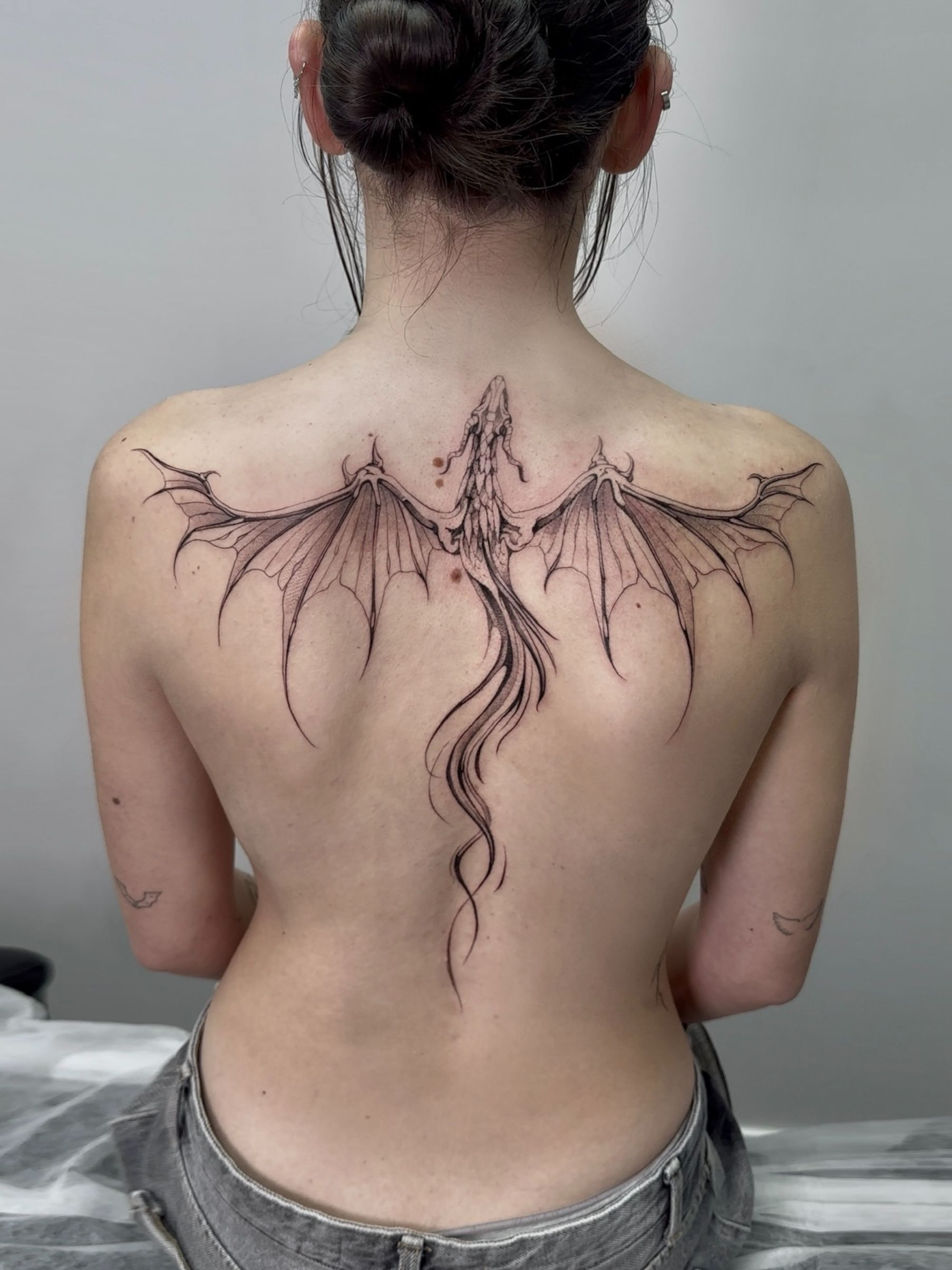 Mujer con un tatuaje en la espalda de un dragón detallado con alas extendidas.