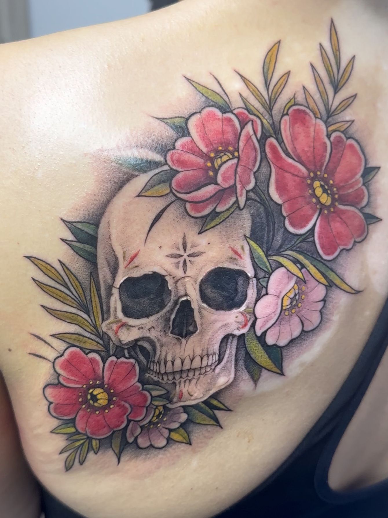 Tatuaje de calavera con flores rojas y rosas y hojas verdes en la espalda.