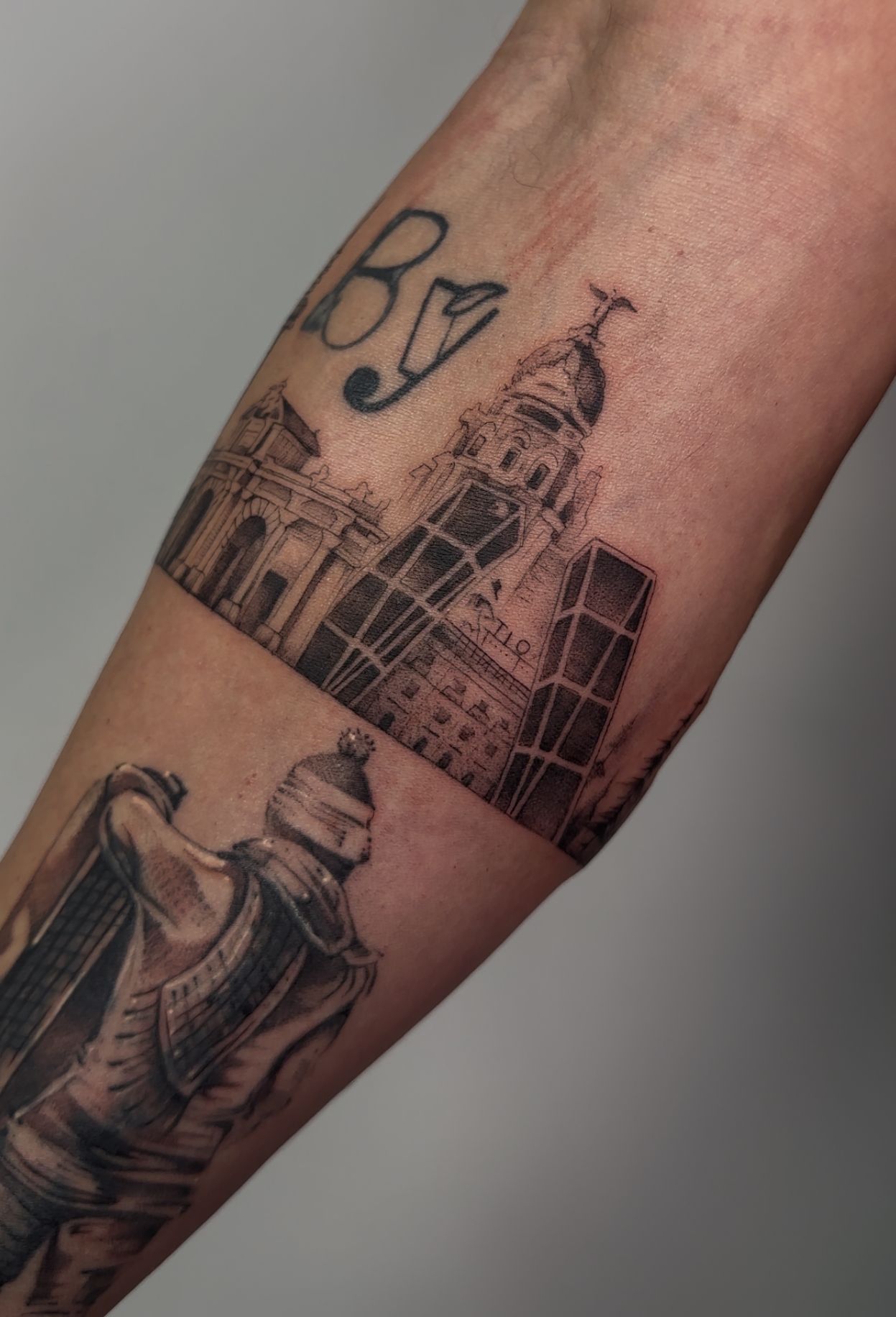 Tatuaje en el brazo que representa un horizonte de edificios con la palabra 