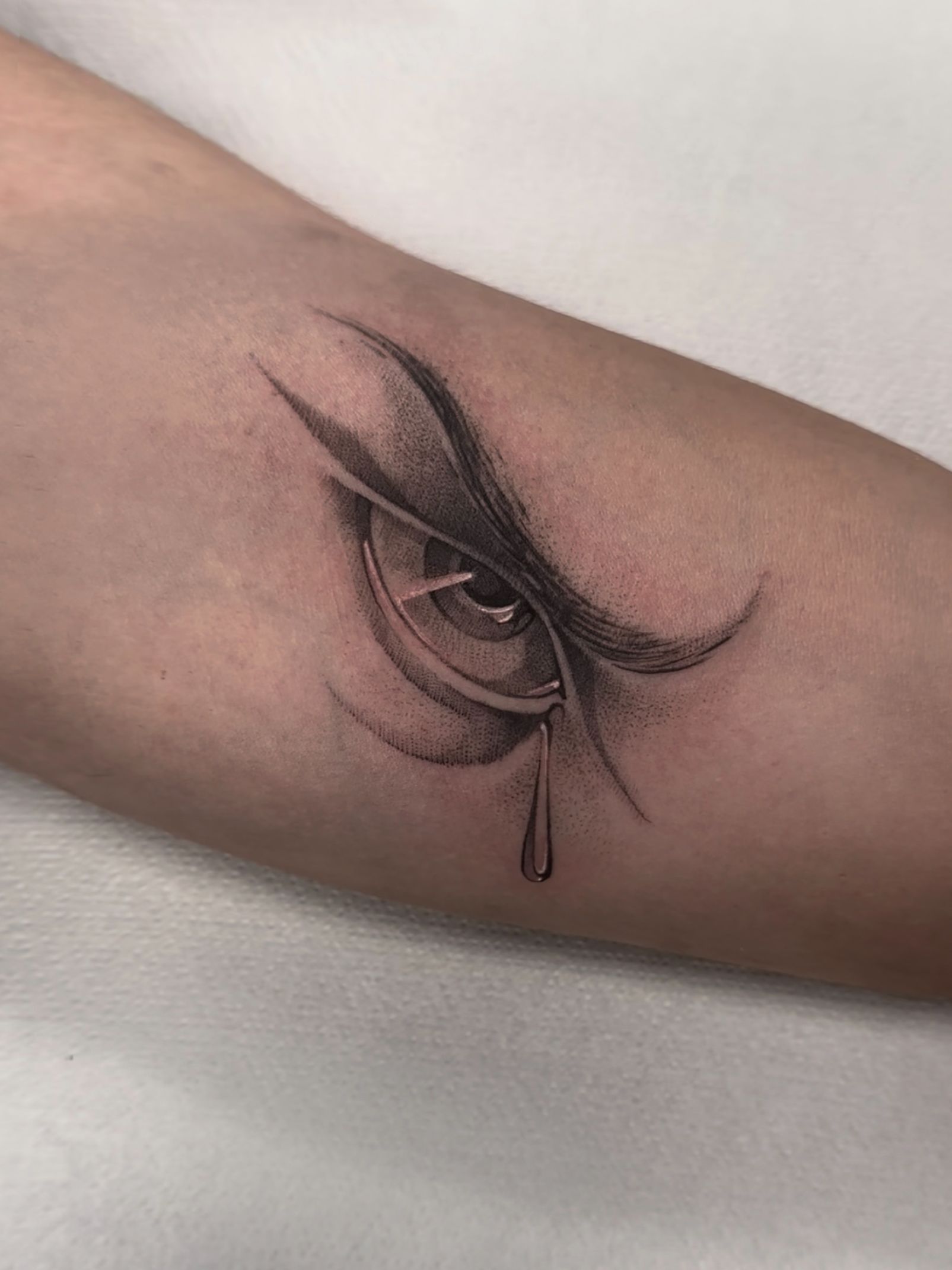 Tatuaje de un ojo detallado en escala de grises con una lágrima en el brazo. Enfoque en el ojo y el sombreado.
