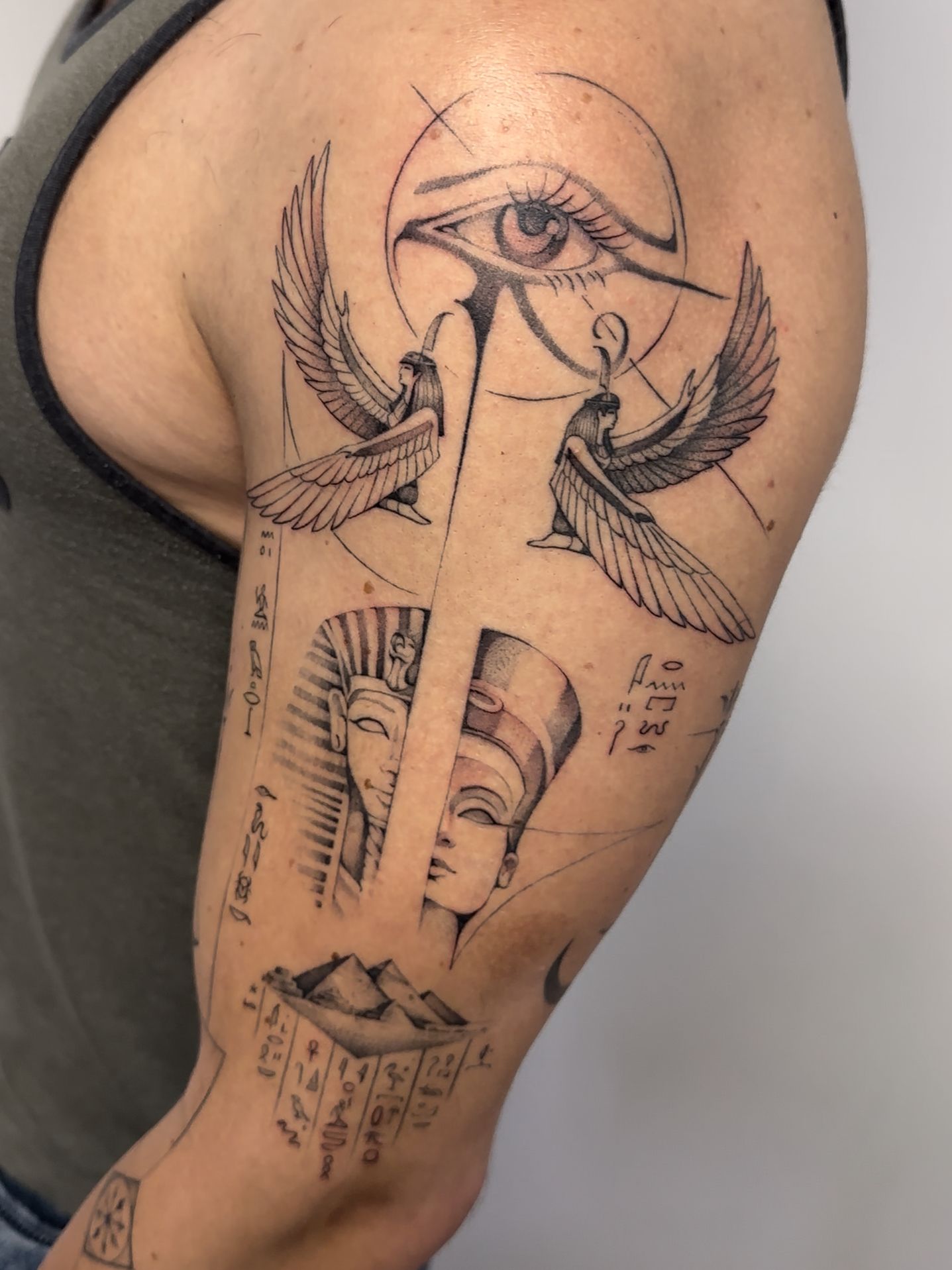 Tatuaje de un diseño de temática egipcia: ojo, alas, faraones y pirámides, en un brazo.