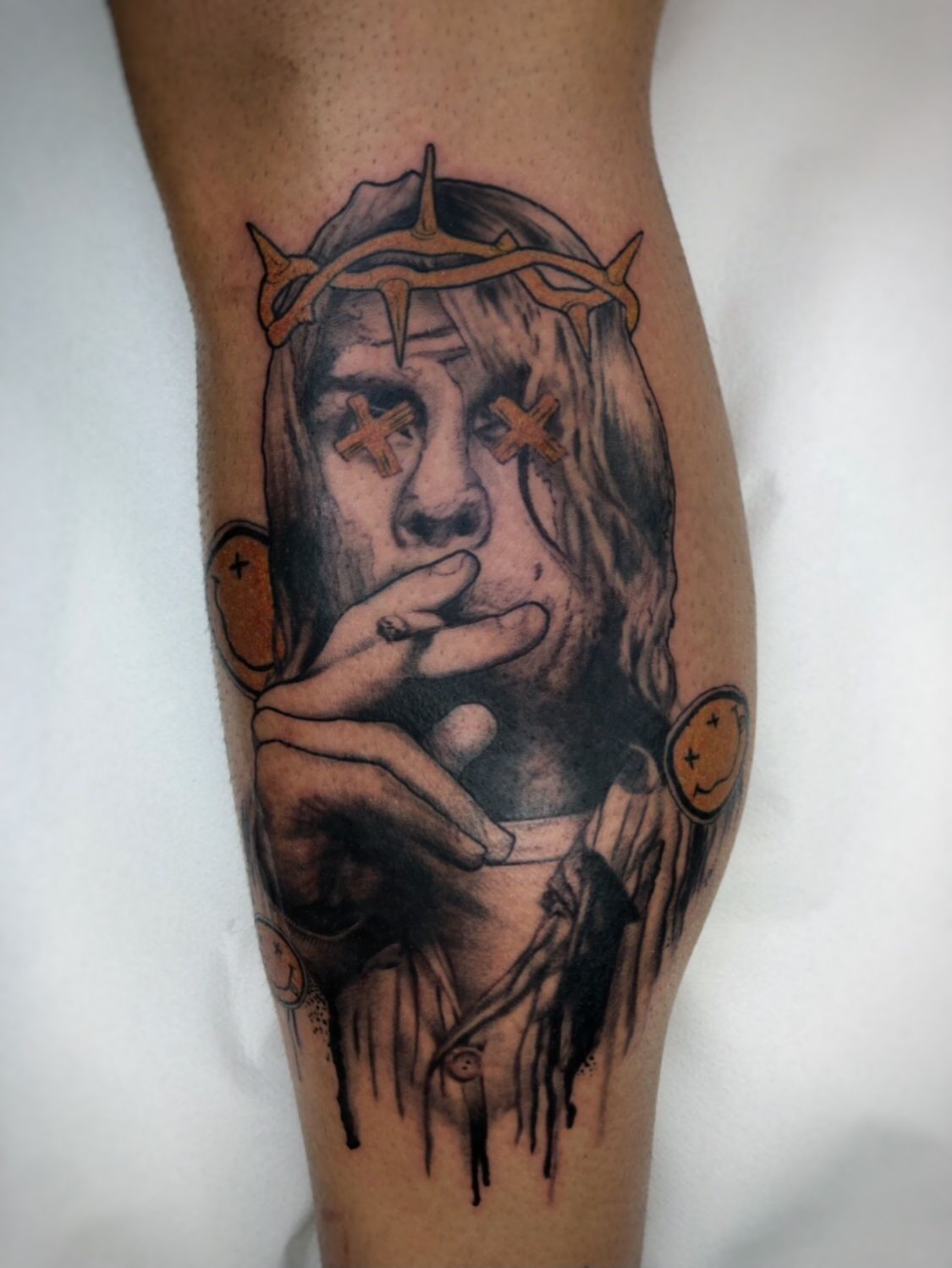 Tatuaje de una persona con una corona de espinas, fumando un cigarrillo, con dos caras sonrientes a los lados.