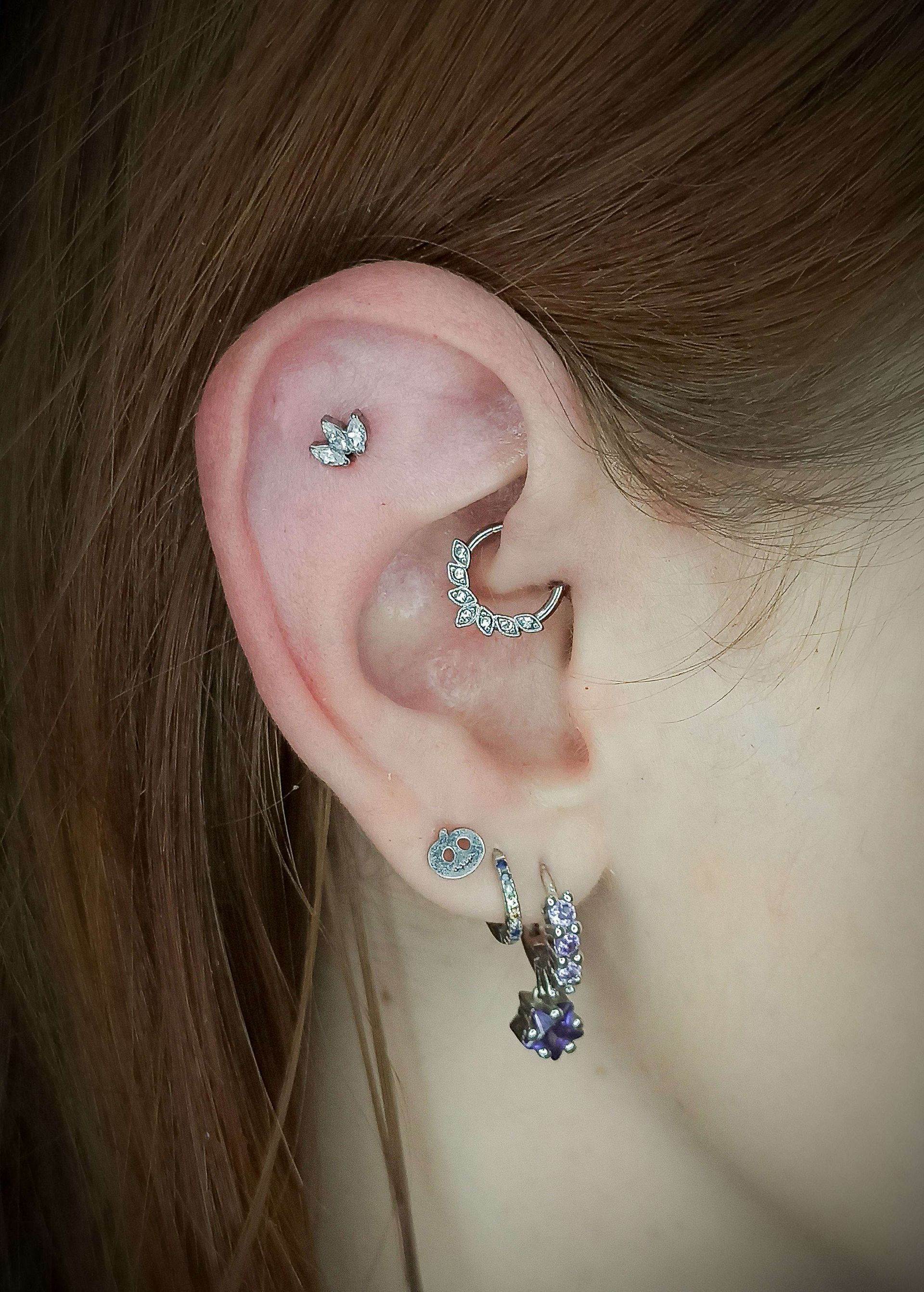 Oreja con múltiples perforaciones, incluidas una hélice, una daith y dos perforaciones en el lóbulo, todas con joyas de plata.