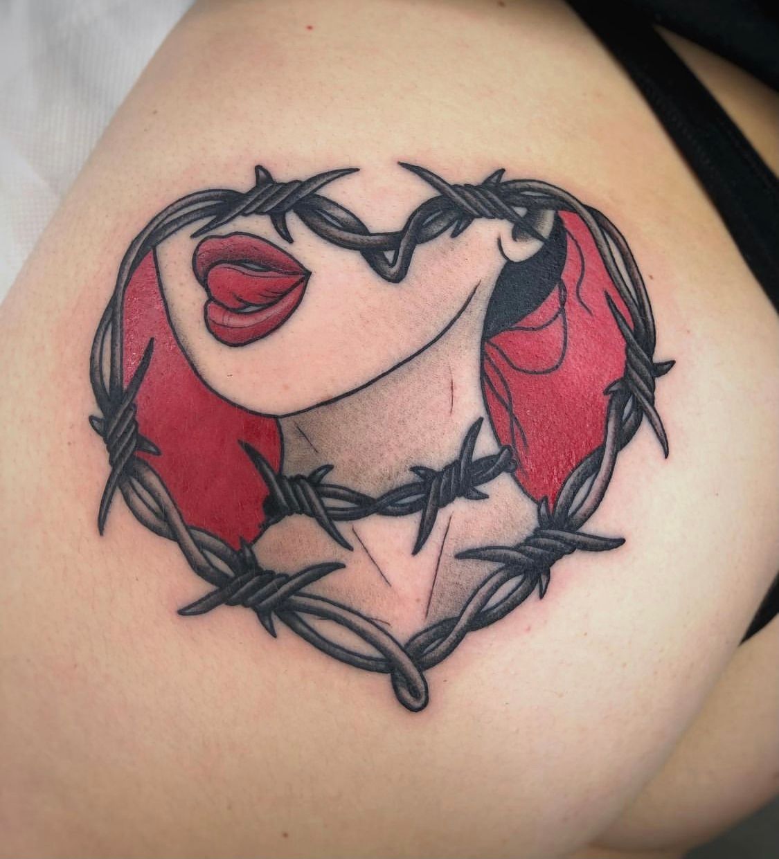 Tatuaje en forma de corazón de labios que sobresalen de la lengua y el cuello, rodeado de alambre de púas, sobre piel clara.