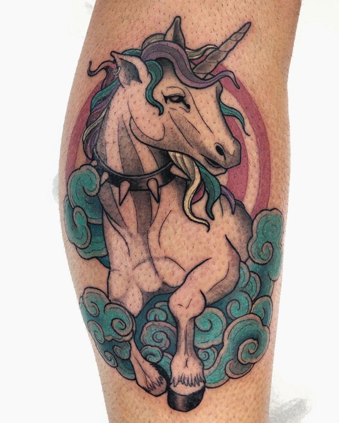 Tatuaje de un unicornio con un collar tachonado de color negro, que emerge de nubes de color verde azulado y contrasta con un círculo rosa.