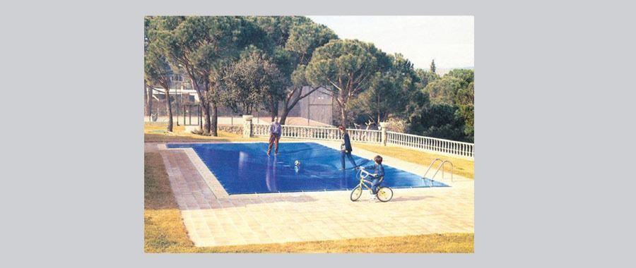 Un hombre en silla de ruedas va en bicicleta cerca de una piscina rodeada de árboles.