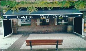 Un café con un toldo negro y un banco delante.