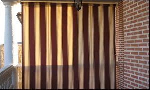 Un toldo de rayas marrones y tostadas cuelga de una pared de ladrillos.