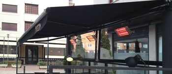 Un restaurante con toldo negro y calentadores en el patio.