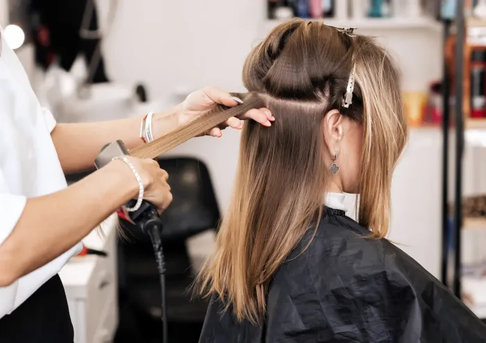 Estilista del cabello usando una plancha sobre el cabello de un cliente en un salón.