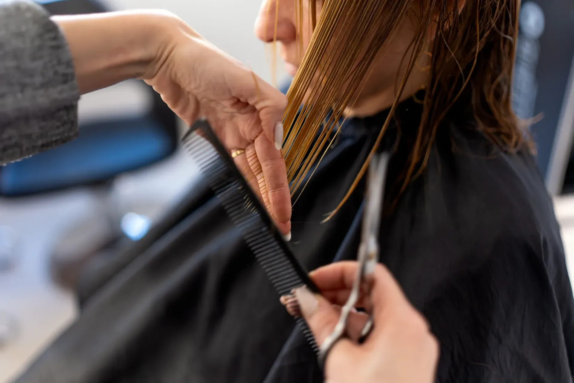 Una peluquera peina el cabello mojado en un salón. Hay otras personas al fondo.