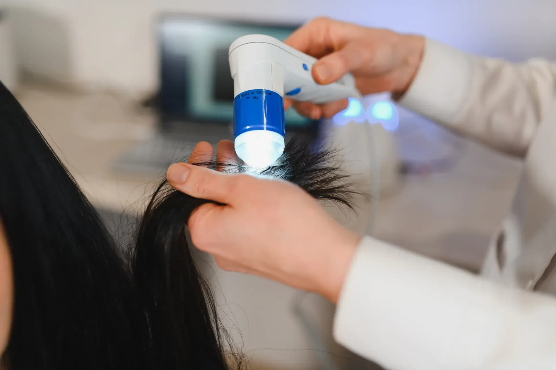 Mujer recibiendo un tratamiento capilar en una peluquería, sonriendo. El estilista aplica aceite con un gotero. 
