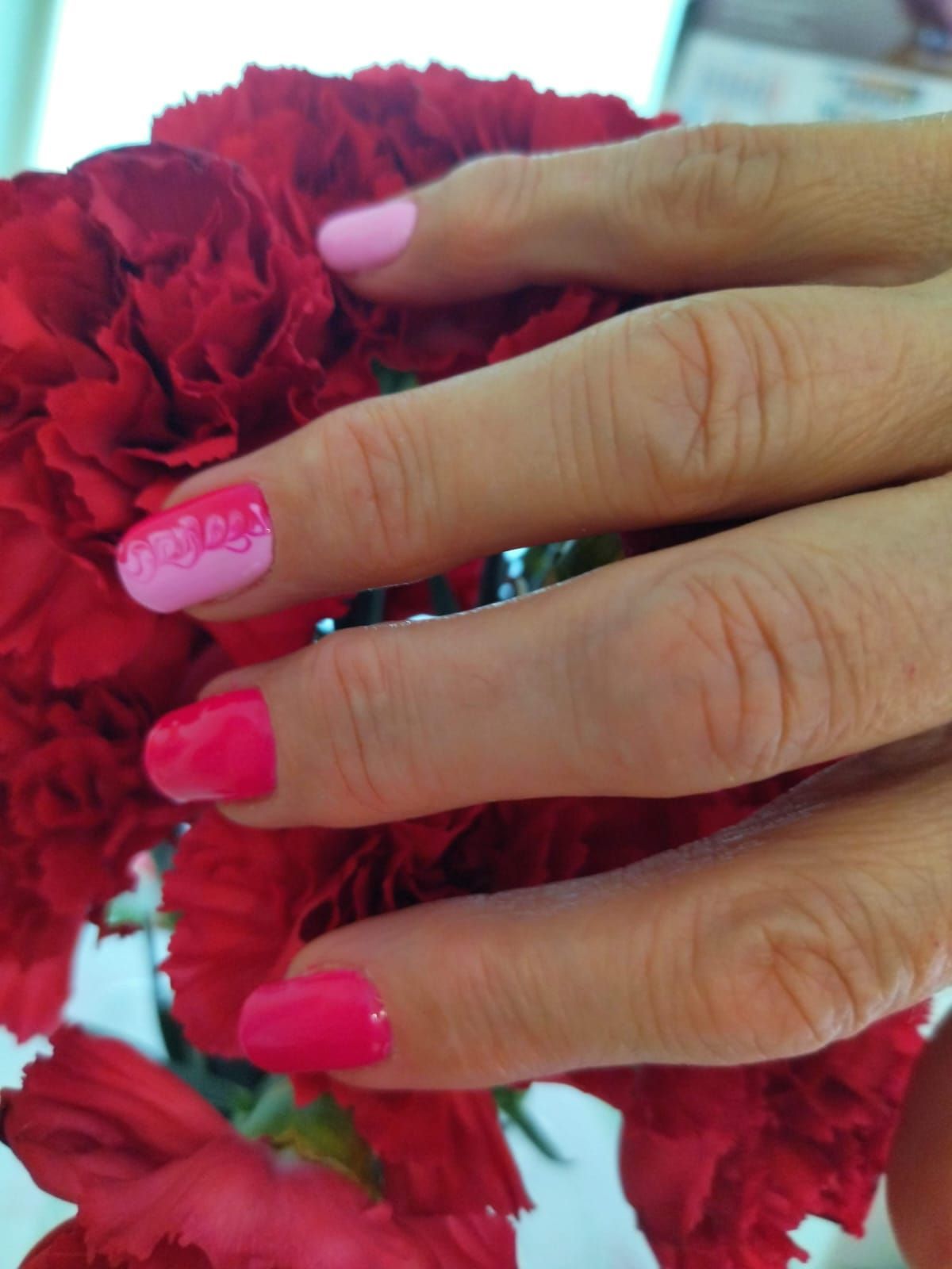 Mano con uñas pintadas de color rosa y magenta, tocando flores rojas.
