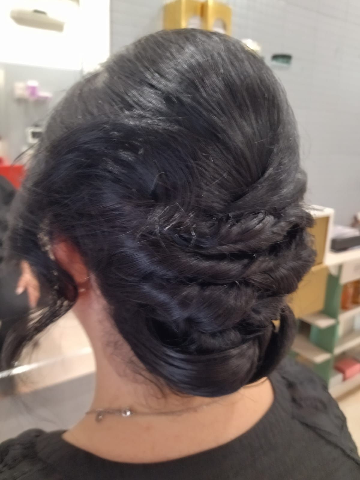 Woman with dark hair in an updo style, with strands woven into a bun at the nape of the neck.