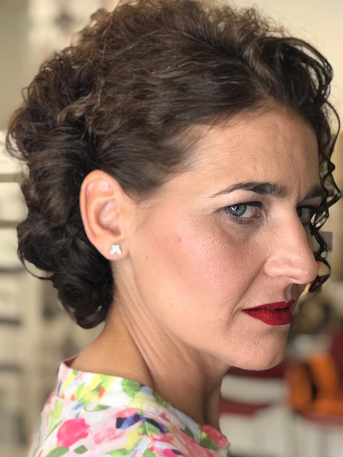 Mujer con cabello castaño rizado, con lápiz labial rojo y una camisa floreada.