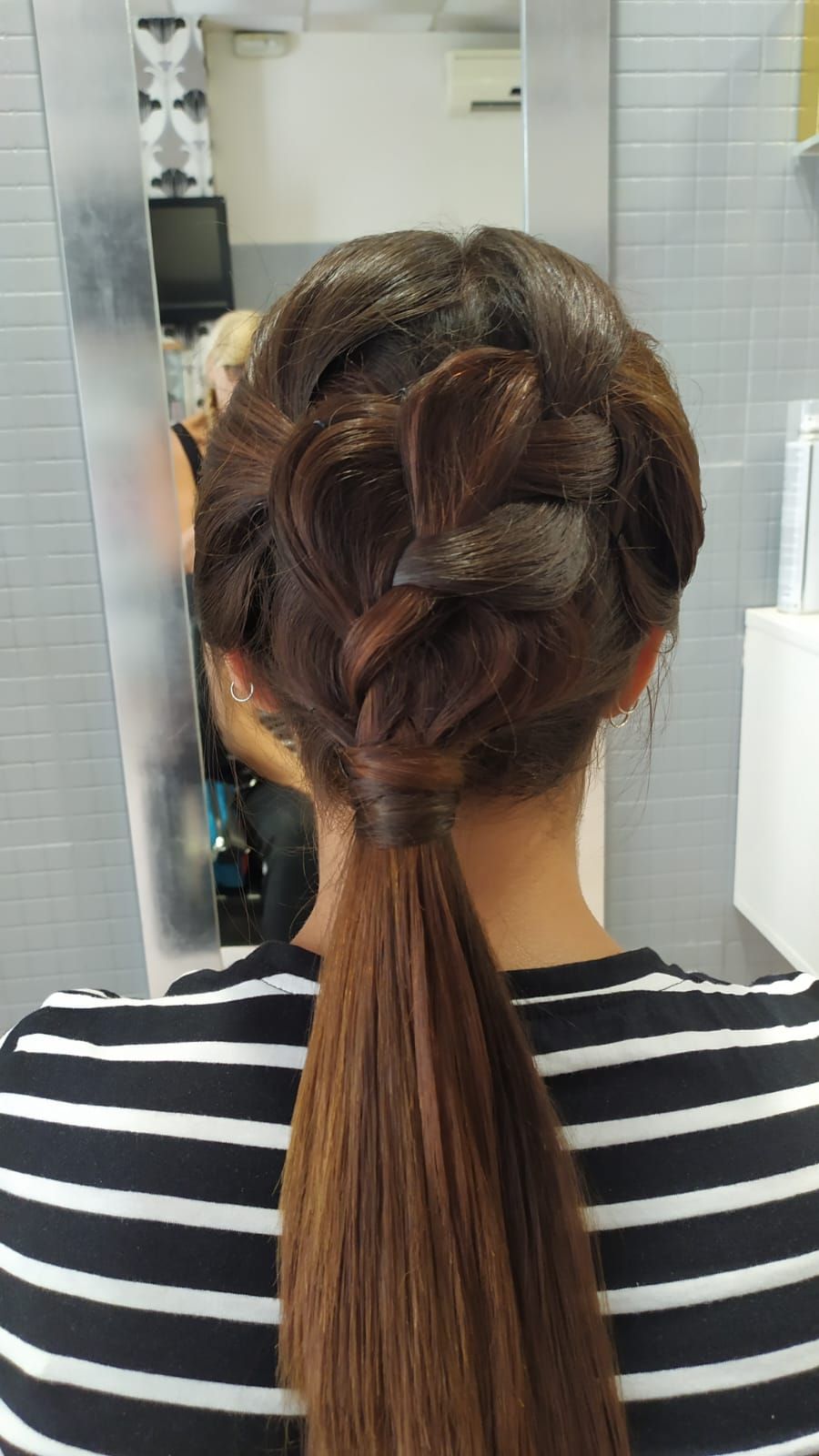 Mujer con cabello castaño peinado en un recogido con trenza y cola de caballo, en un salón.