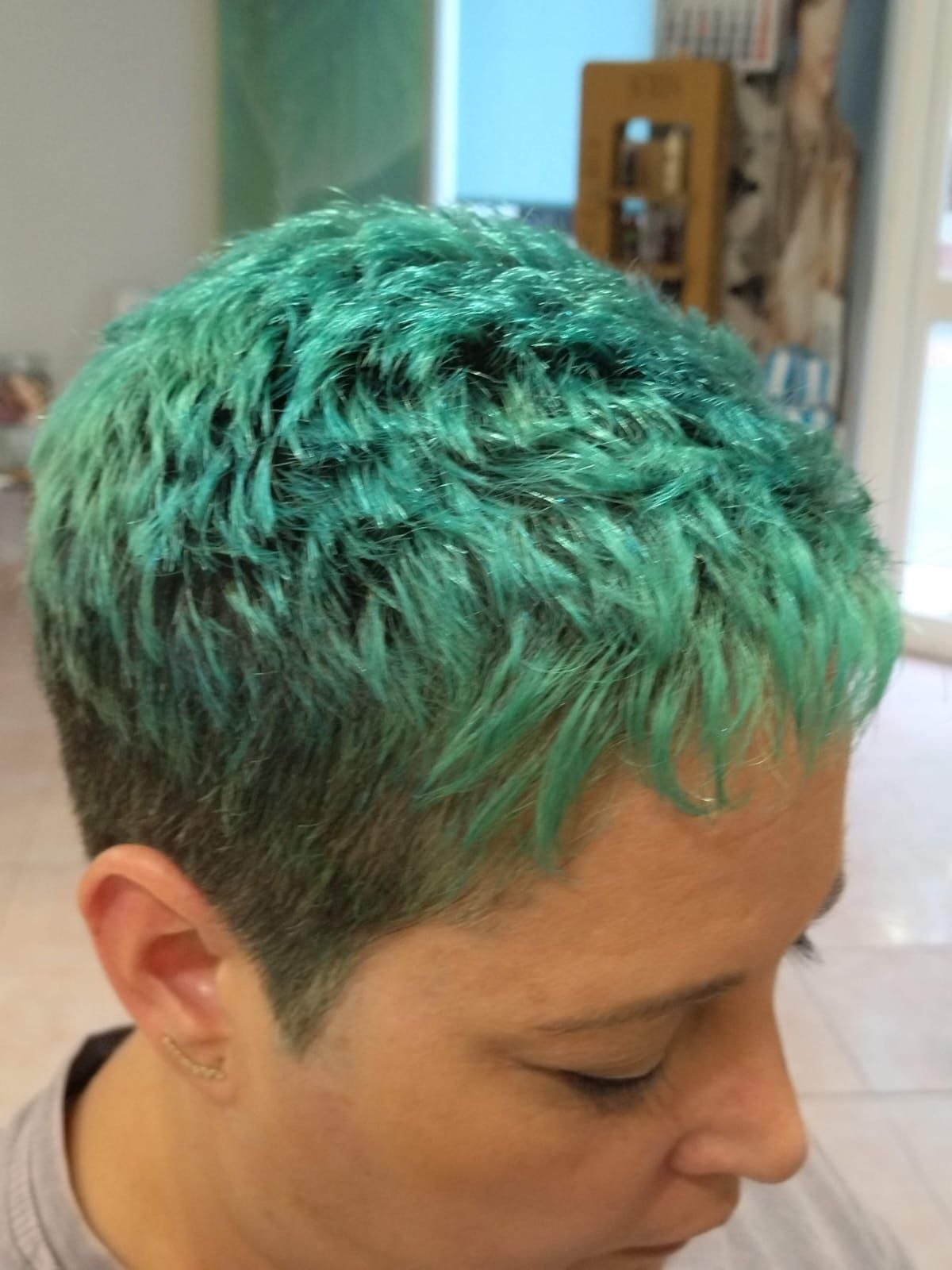 Persona con cabello corto de color verde azulado; vista lateral en el interior.