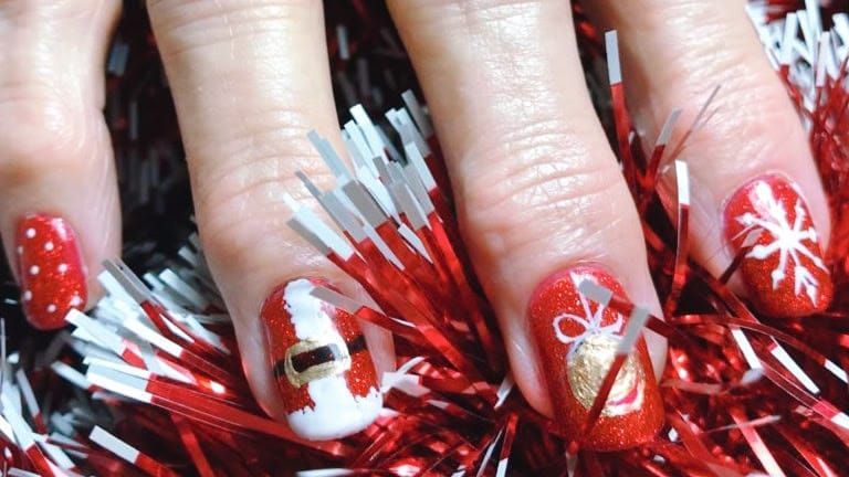 Arte de uñas con temática navideña en color rojo: Papá Noel, copo de nieve, lunares y una campana sobre un fondo brillante.